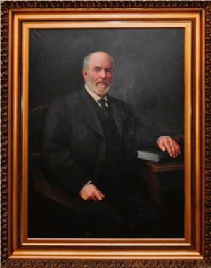 Painting of a balding white man with a salt and pepper beard. He is wearing a suit, waistcoat, and tie, and has one hand in his lap, another resting on a large book. 